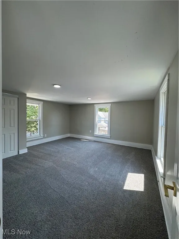Empty room featuring dark carpet and baseboards