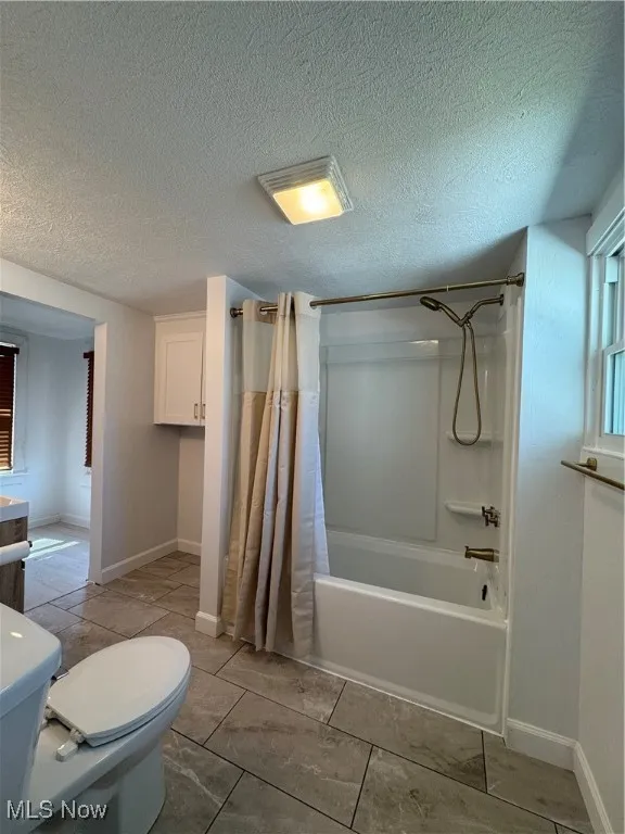 Full bathroom with shower / bath combo with shower curtain, a textured ceiling, light tile patterned floors, and vanity