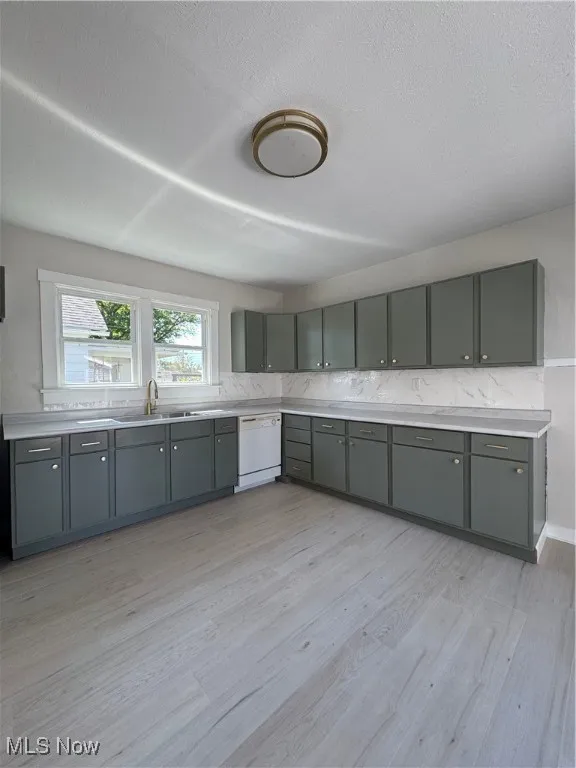 Kitchen featuring light countertops, light wood-style floors, backsplash, gray cabinetry, and a textured ceiling