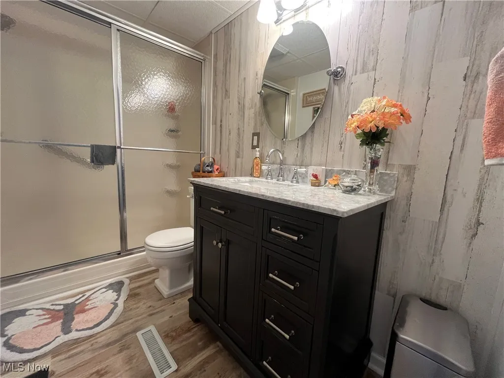 Bathroom featuring vanity, a stall shower, light wood-style floors, and wooden walls