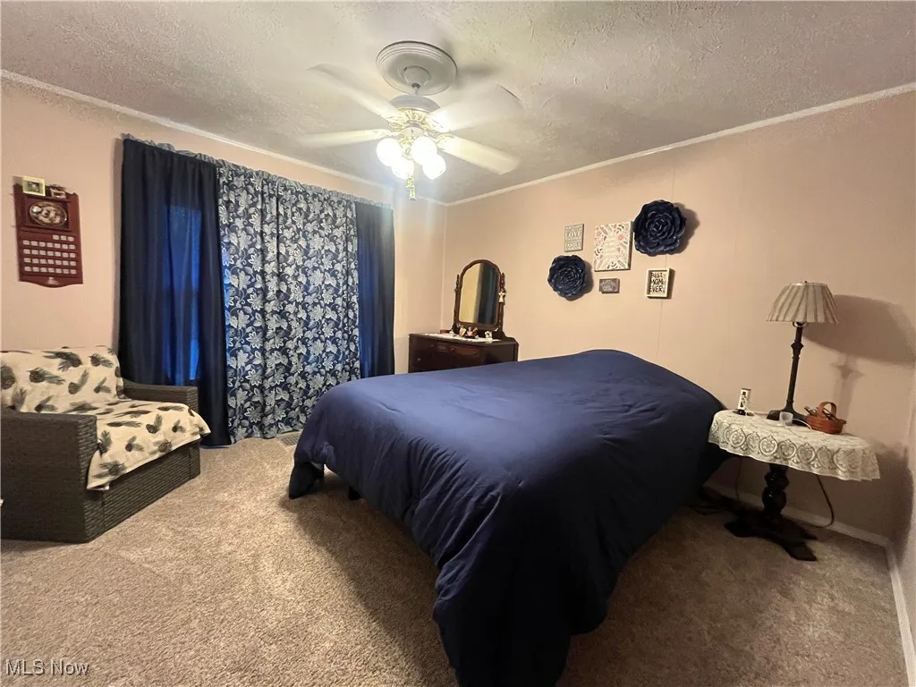 Carpeted bedroom featuring a textured ceiling, a ceiling fan, and crown molding