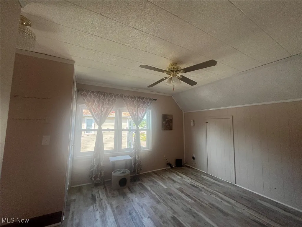 Bonus room with wood finished floors, lofted ceiling, ceiling fan, a textured ceiling, and wooden walls