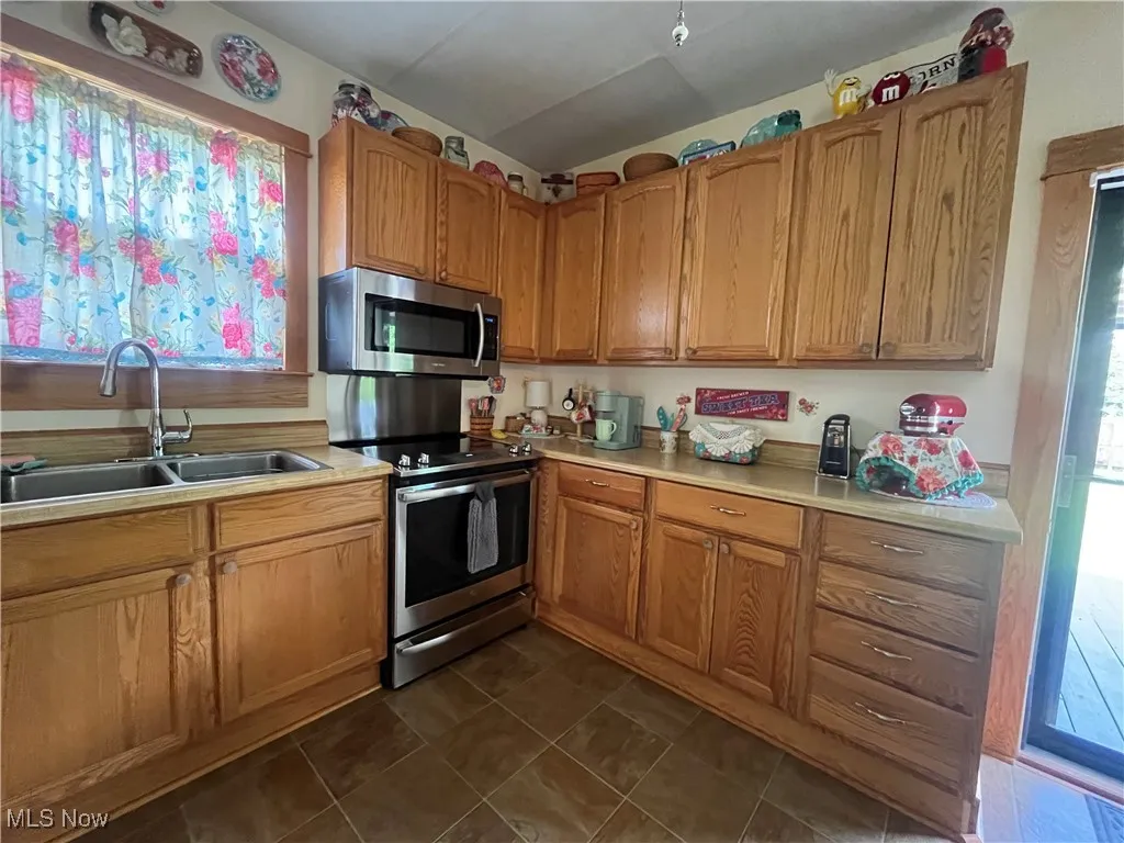Kitchen featuring stainless steel appliances, light countertops, brown cabinets, and dark tile patterned floors