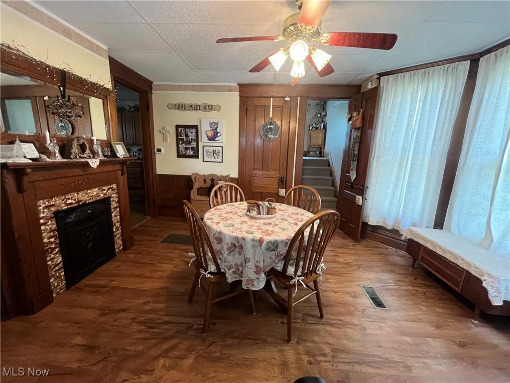 Dining space with dark wood-type flooring, a tiled fireplace, wainscoting, stairway, and a drop ceiling