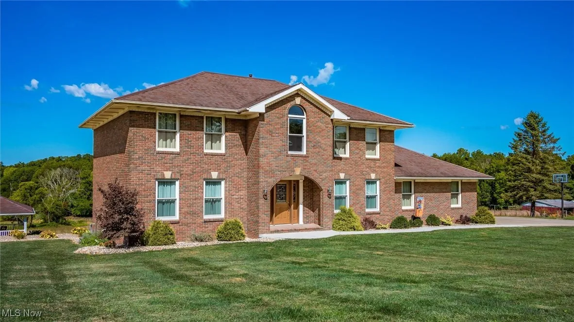 Colonial home featuring a front yard, brick siding, and a shingled roof