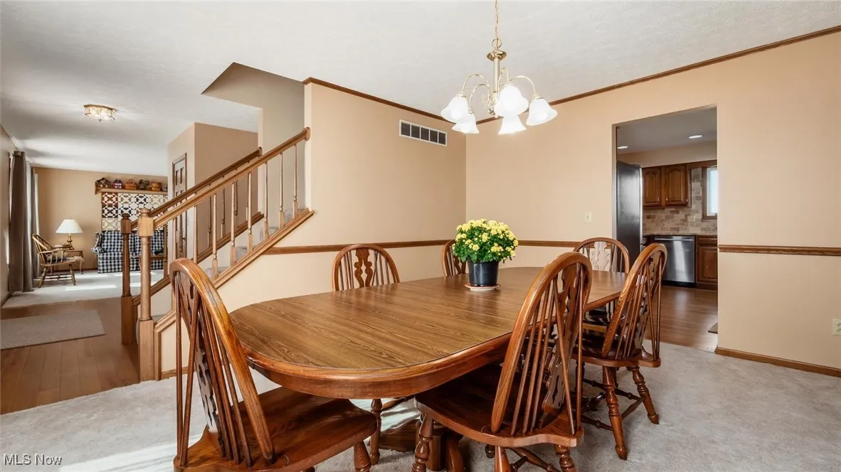 Dining room with a chandelier, light colored carpet, light wood-style flooring, stairs, and ornamental molding