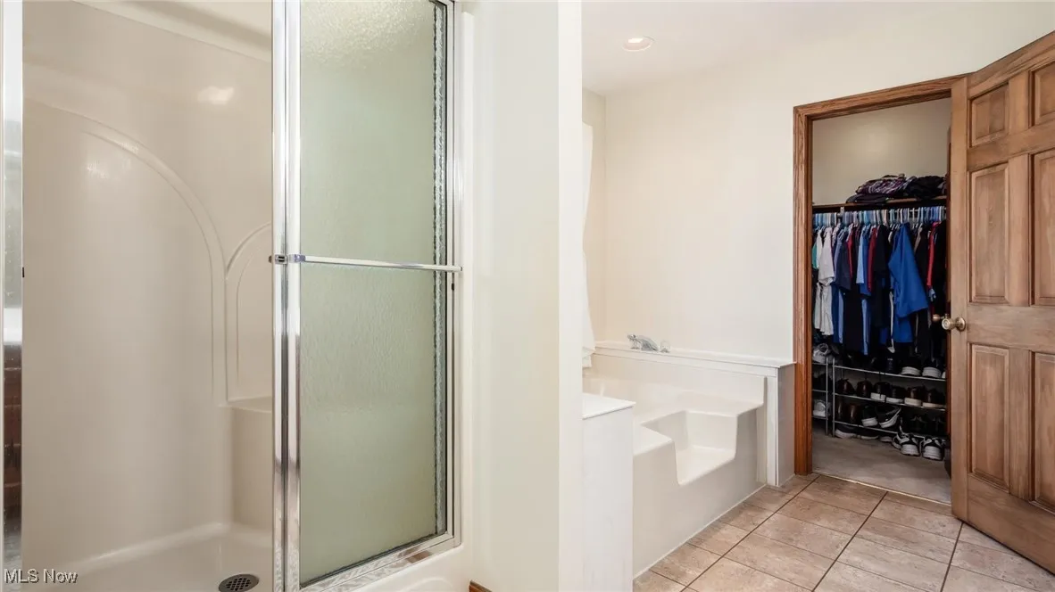 Bathroom with a stall shower, light tile patterned floors, a garden tub, and a walk in closet