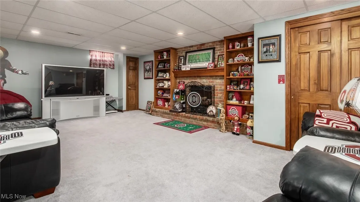 Carpeted living area with a drop ceiling and a brick fireplace