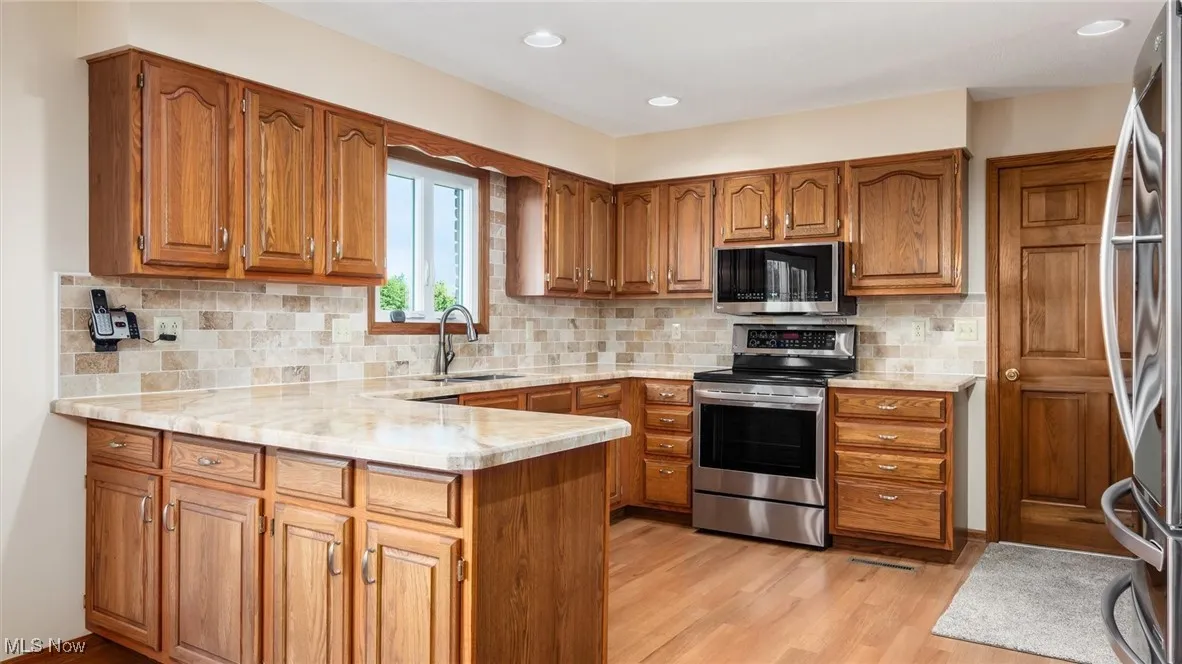 Kitchen with brown cabinets, stainless steel appliances, a peninsula, and recessed lighting