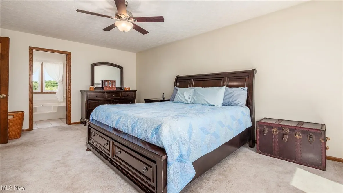 Bedroom featuring a ceiling fan, light colored carpet, a textured ceiling, and ensuite bathroom