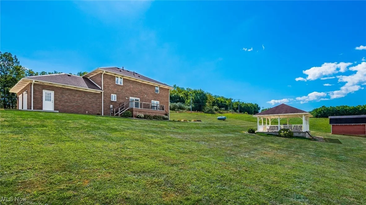 View of green lawn with a wooden deck, a gazebo, and an attached garage