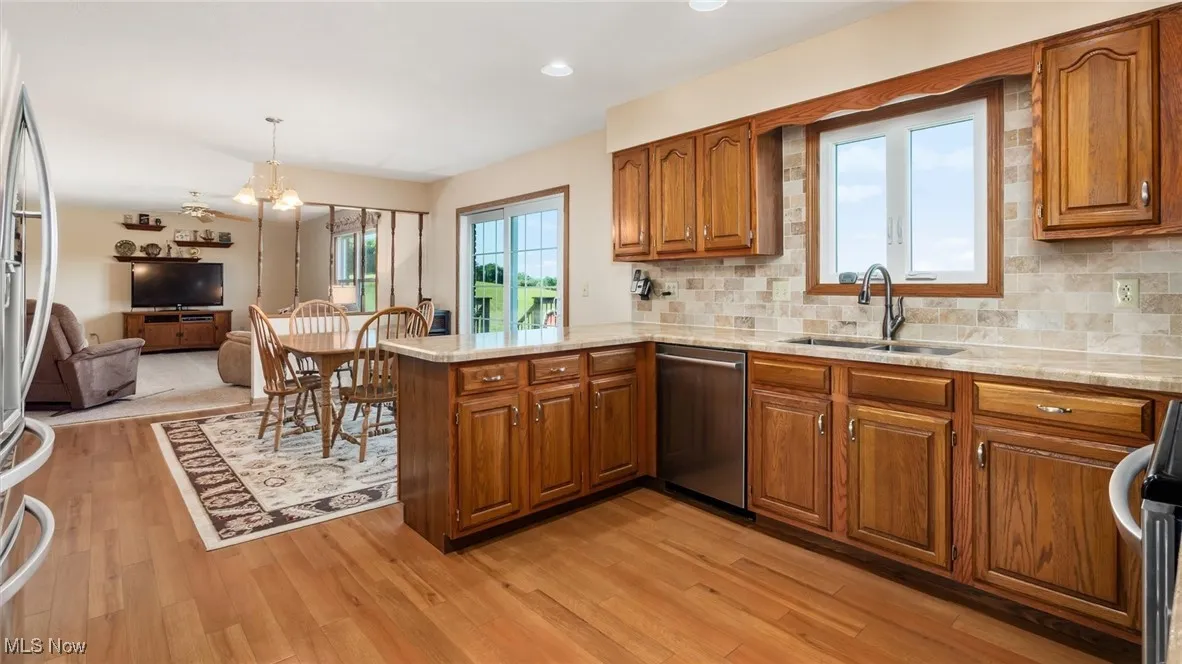 Kitchen featuring brown cabinetry, tasteful backsplash, light stone countertops, a chandelier, and recessed lighting