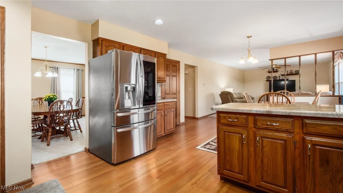 Kitchen with a chandelier, decorative light fixtures, stainless steel refrigerator with ice dispenser, brown cabinetry, and recessed lighting