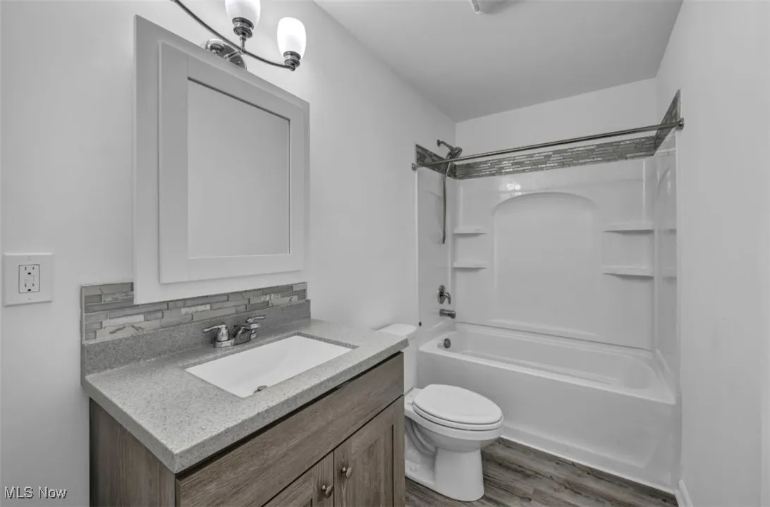 Full bath featuring washtub / shower combination, vanity, backsplash, and light wood-type flooring