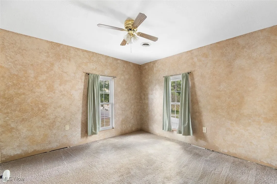 Empty room with ceiling fan, carpet, and a textured wall
