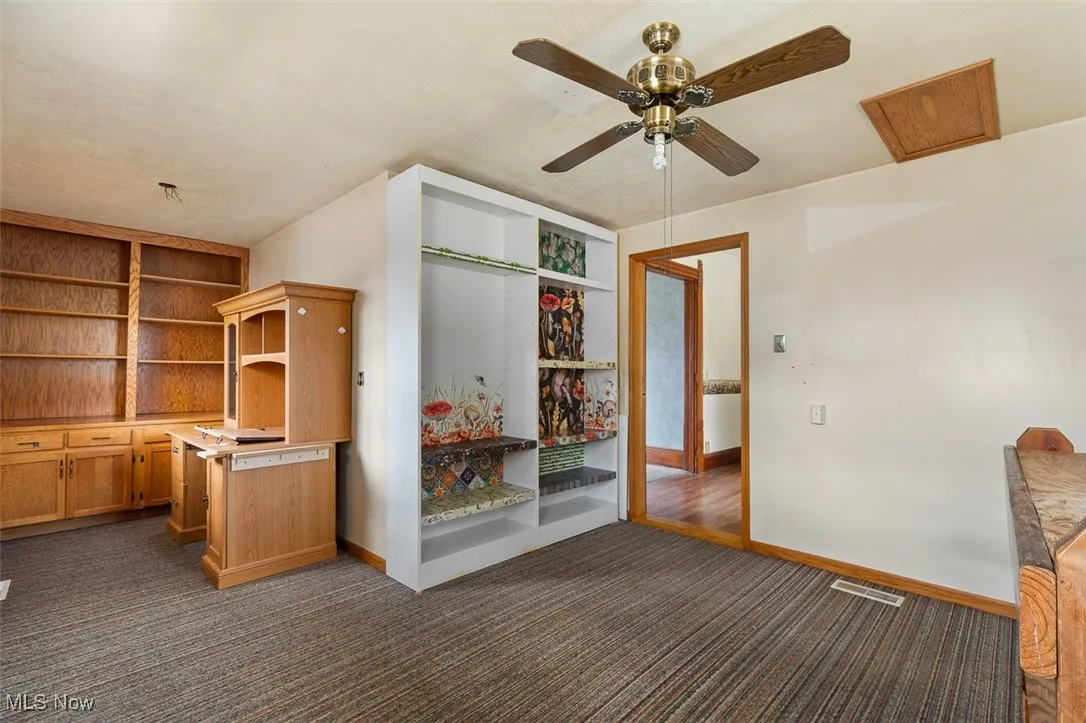 Unfurnished office with dark colored carpet, a ceiling fan, and built in features
