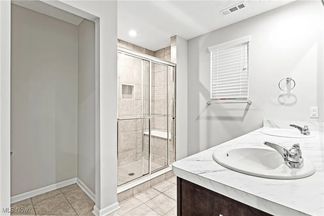 Bathroom with a shower stall, light tile patterned flooring, and double vanity