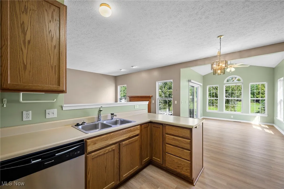 Kitchen with a peninsula, open floor plan, dishwasher, light wood-style flooring, and brown cabinetry