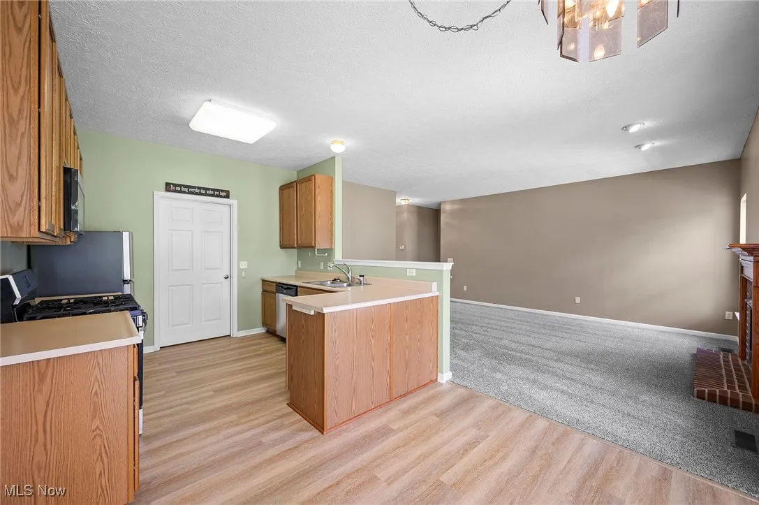 Kitchen with a peninsula, light countertops, open floor plan, brown cabinets, and range with gas stovetop