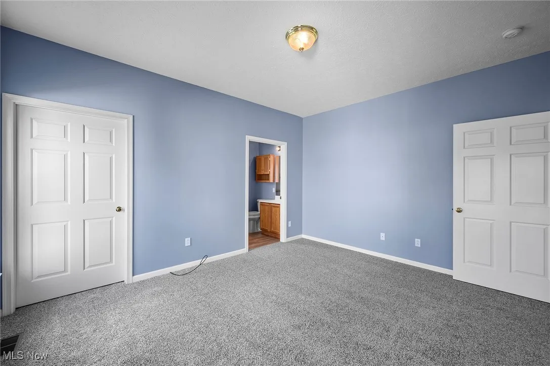 Unfurnished bedroom with connected bathroom and carpet flooring