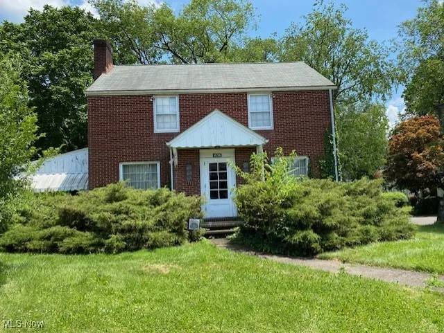 View of front facade with a chimney, brick siding, and a front lawn