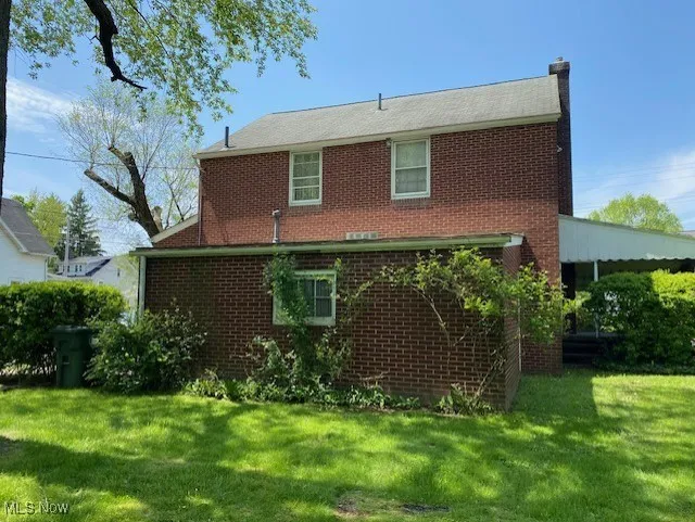 Rear view of house with brick siding, a yard, and a chimney