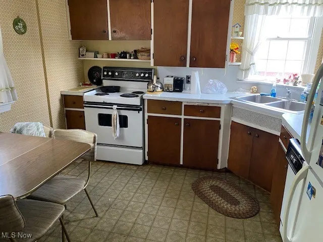 Kitchen with white appliances, light countertops, open shelves, light flooring, and dark brown cabinetry