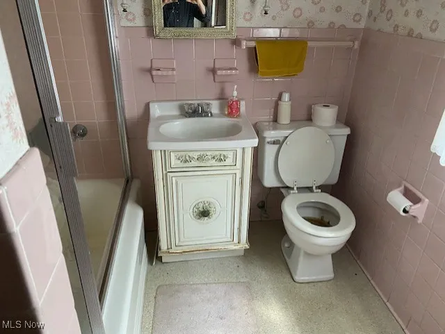 Bathroom with vanity, tile walls, a stall shower, wallpapered walls, and a wainscoted wall
