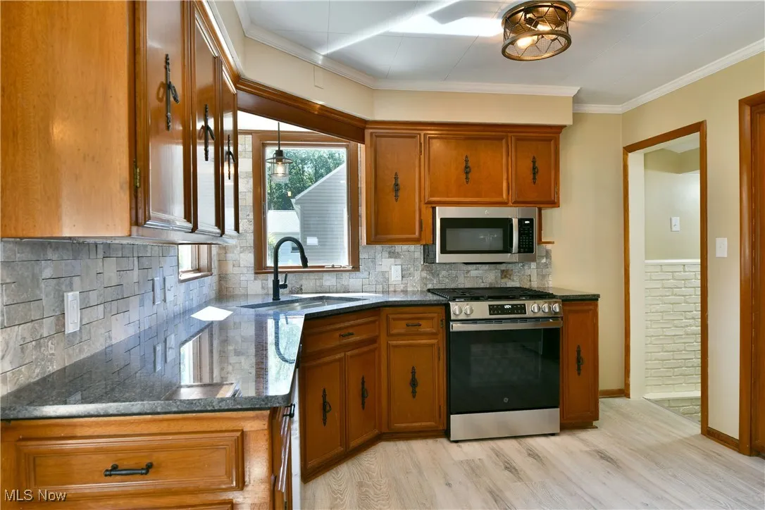 Kitchen featuring brown cabinetry, appliances with stainless steel finishes, light wood-style floors, backsplash, and ornamental molding