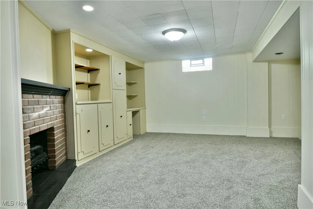 Basement with light carpet, a fireplace, wood walls, and built in shelves