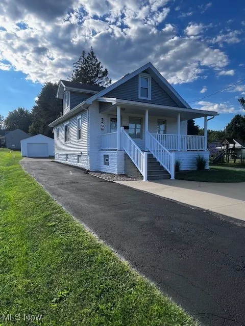 Bungalow-style house with covered porch, an outdoor structure, a garage, driveway, and a front lawn