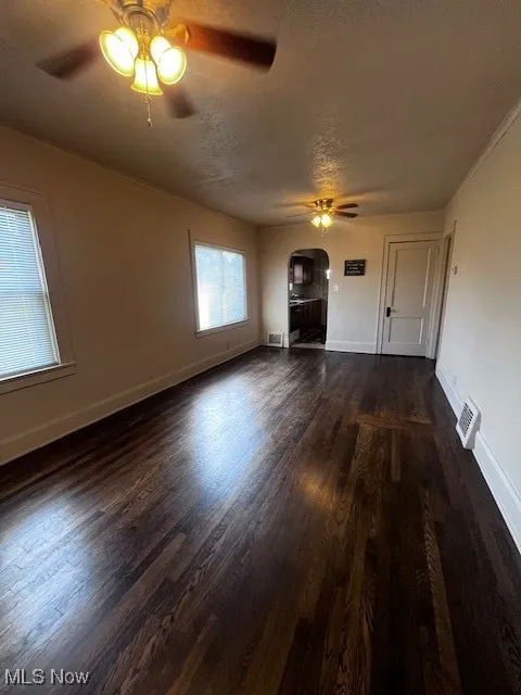 Unfurnished living room with a textured ceiling, dark wood-type flooring, a ceiling fan, crown molding, and arched walkways