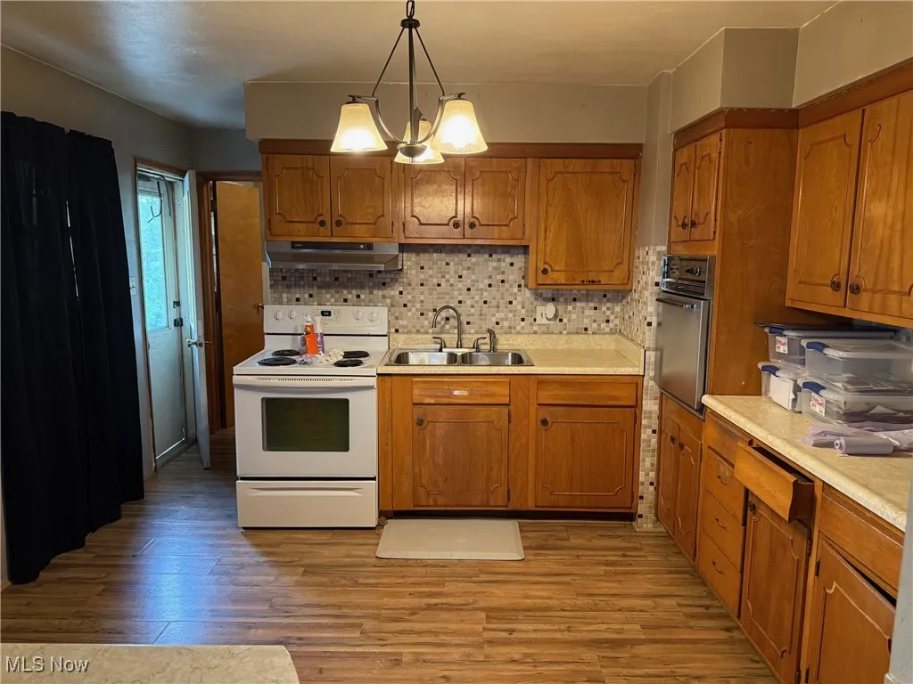 Kitchen with under cabinet range hood, white electric stove, a sink, light wood-type flooring, and oven