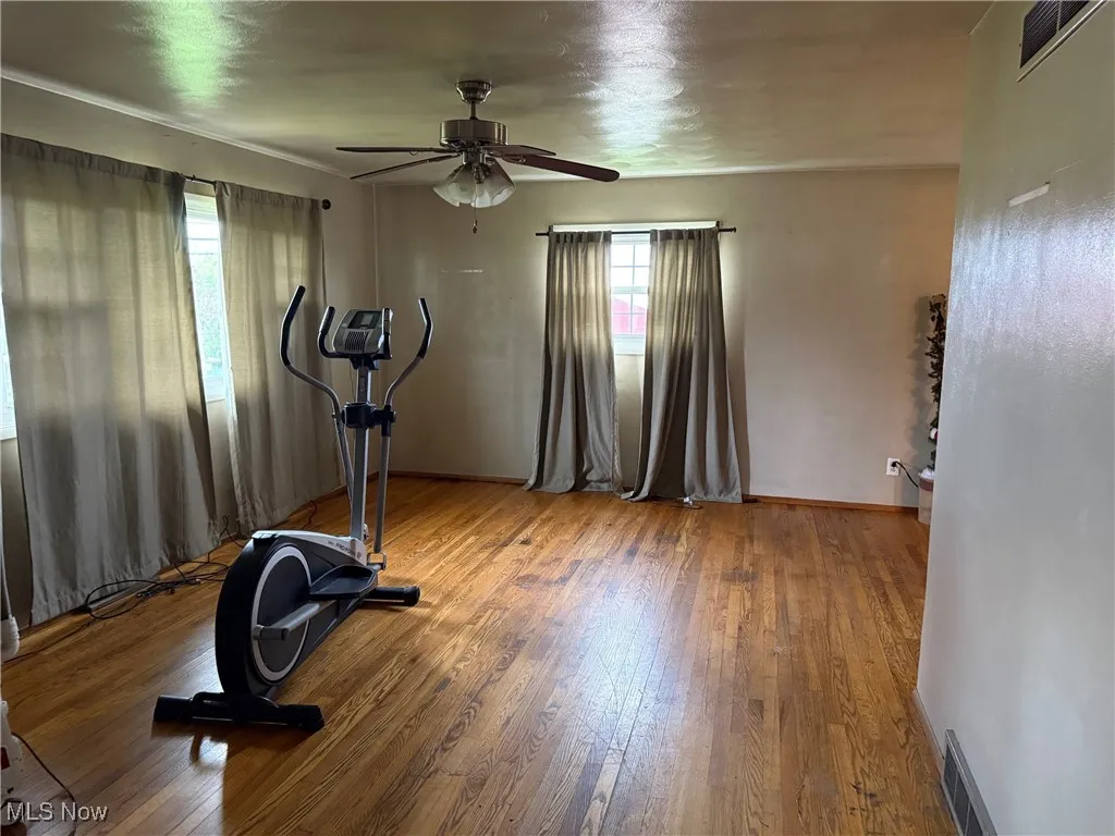 Workout area featuring baseboards, a ceiling fan, visible vents, and wood finished floors