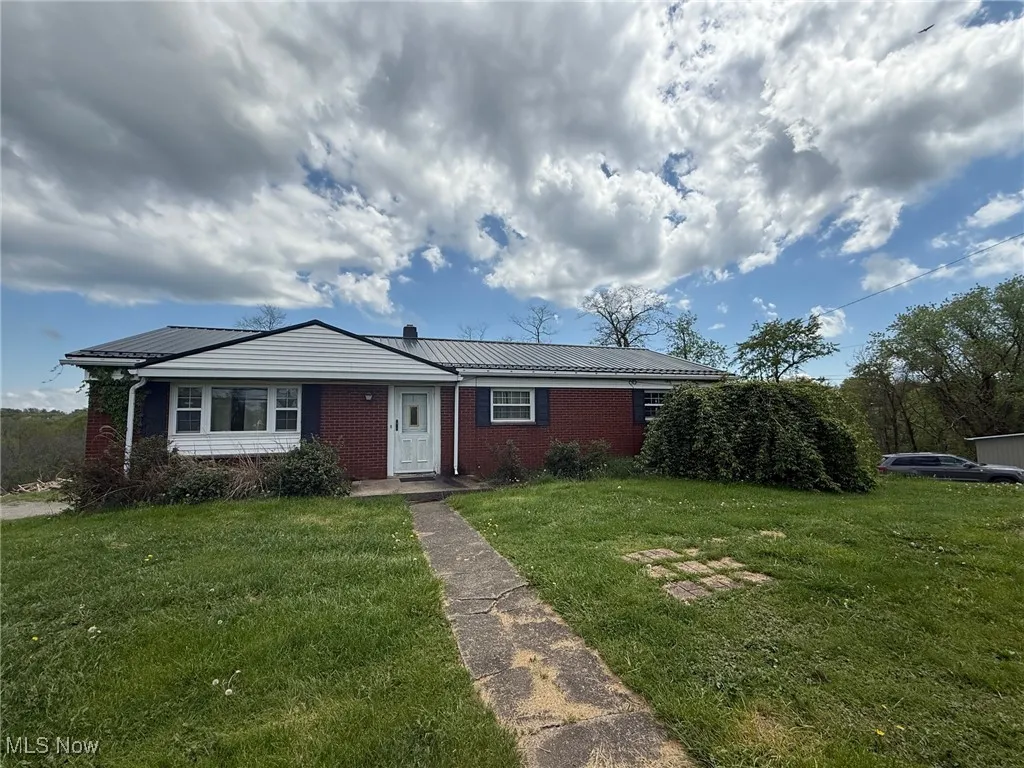 View of front facade featuring metal roof, brick siding, and a front lawn