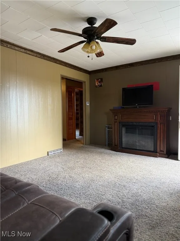 Living room with carpet flooring, a glass covered fireplace, and ceiling fan