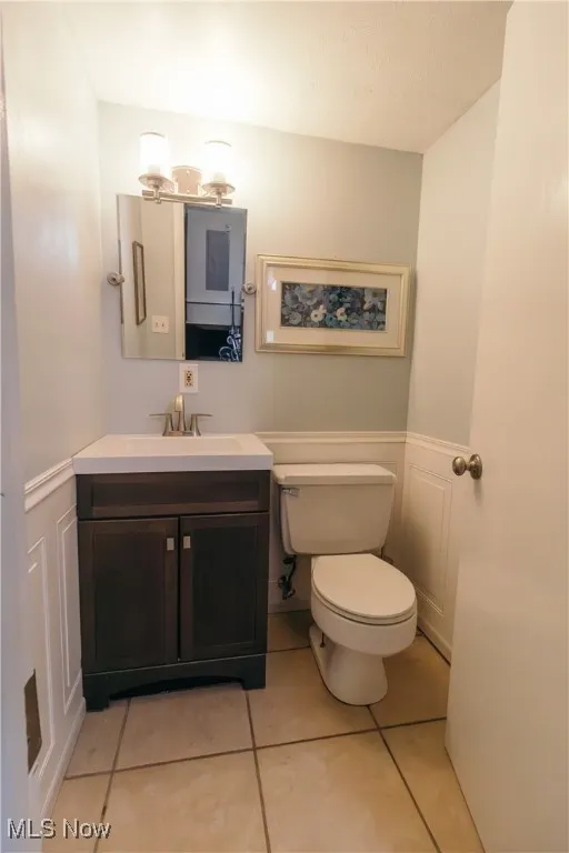 Half bath featuring wainscoting, light tile patterned floors, vanity, and a decorative wall