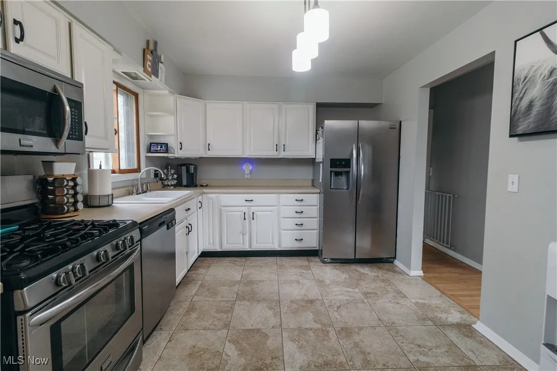 Kitchen with stainless steel appliances, light countertops, white cabinets, light tile patterned flooring, and pendant lighting