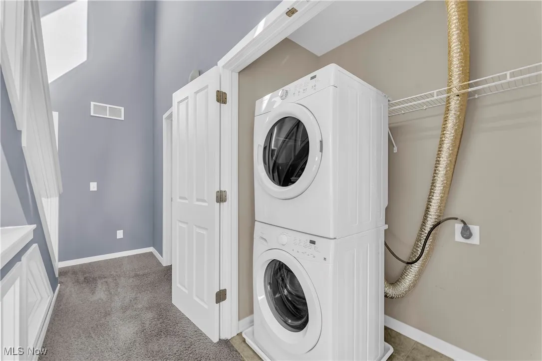 Washroom with stacked washing machine and dryer and light colored carpet