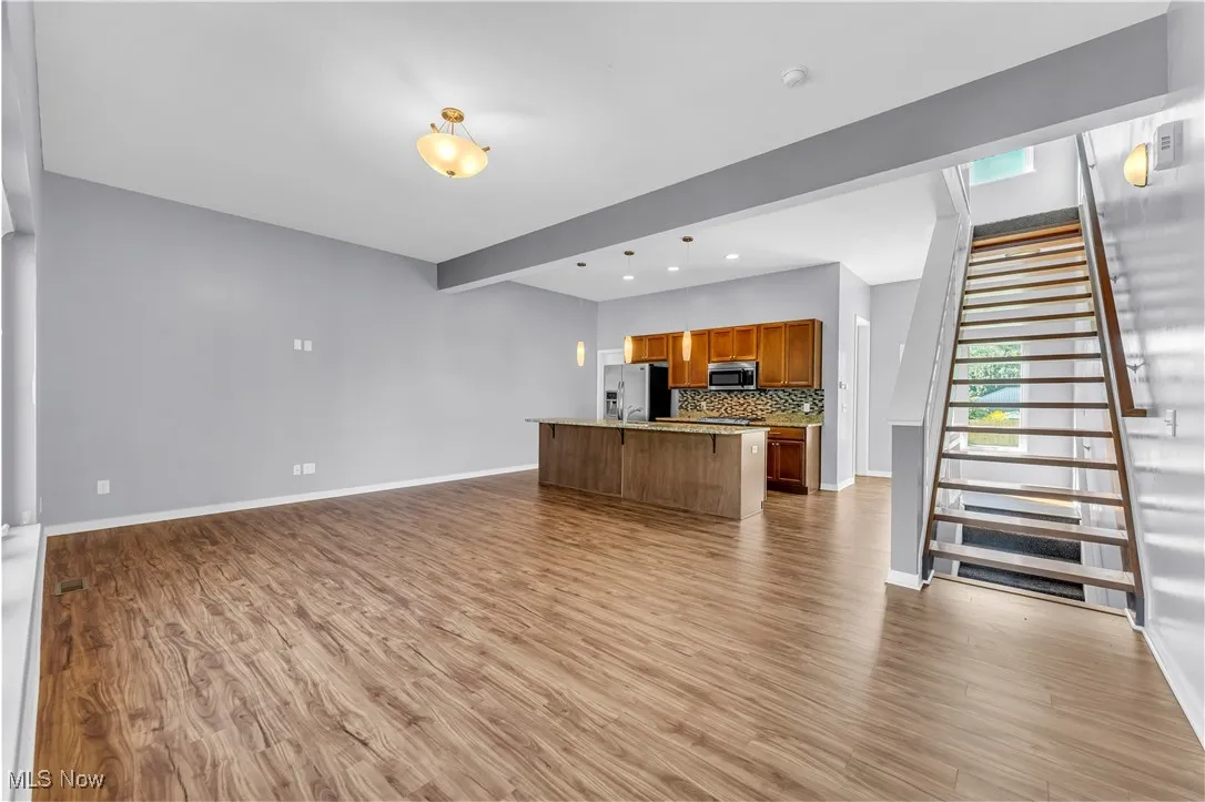 Unfurnished living room featuring beam ceiling, light wood-type flooring, and stairway