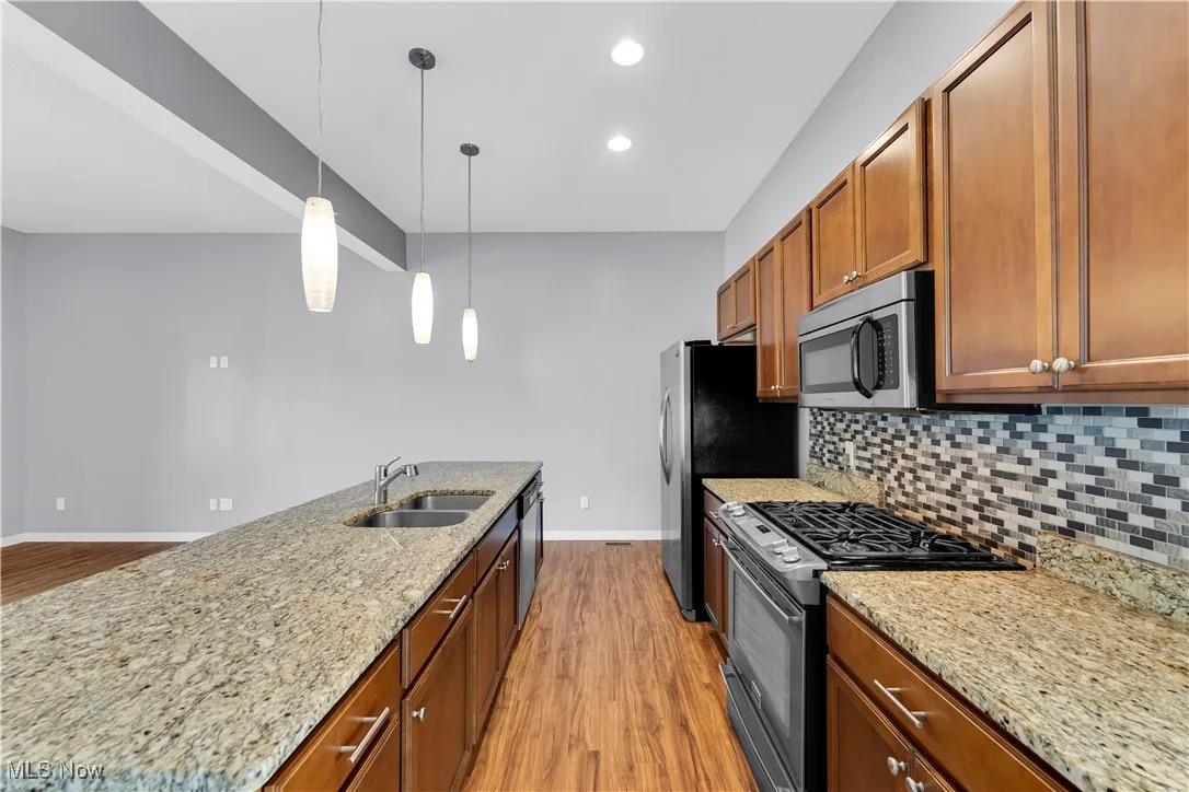Kitchen with stainless steel appliances, light stone countertops, light wood-type flooring, pendant lighting, and a spacious island