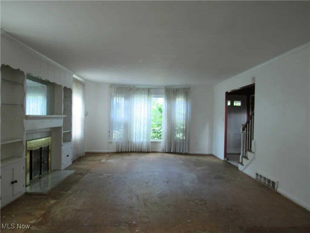 Unfurnished living room featuring a glass covered fireplace, crown molding, and stairs
