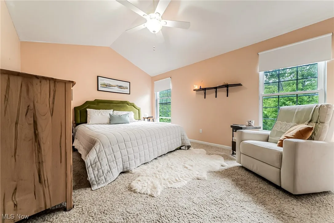 Carpeted bedroom featuring multiple windows, lofted ceiling, and a ceiling fan