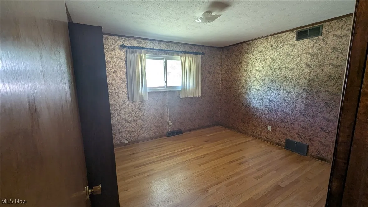 Empty room with light wood-style floors, a textured ceiling, and wallpapered walls