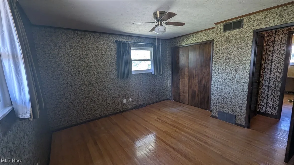 Unfurnished bedroom featuring a textured ceiling, hardwood / wood-style floors, ornamental molding, multiple closets, and ceiling fan