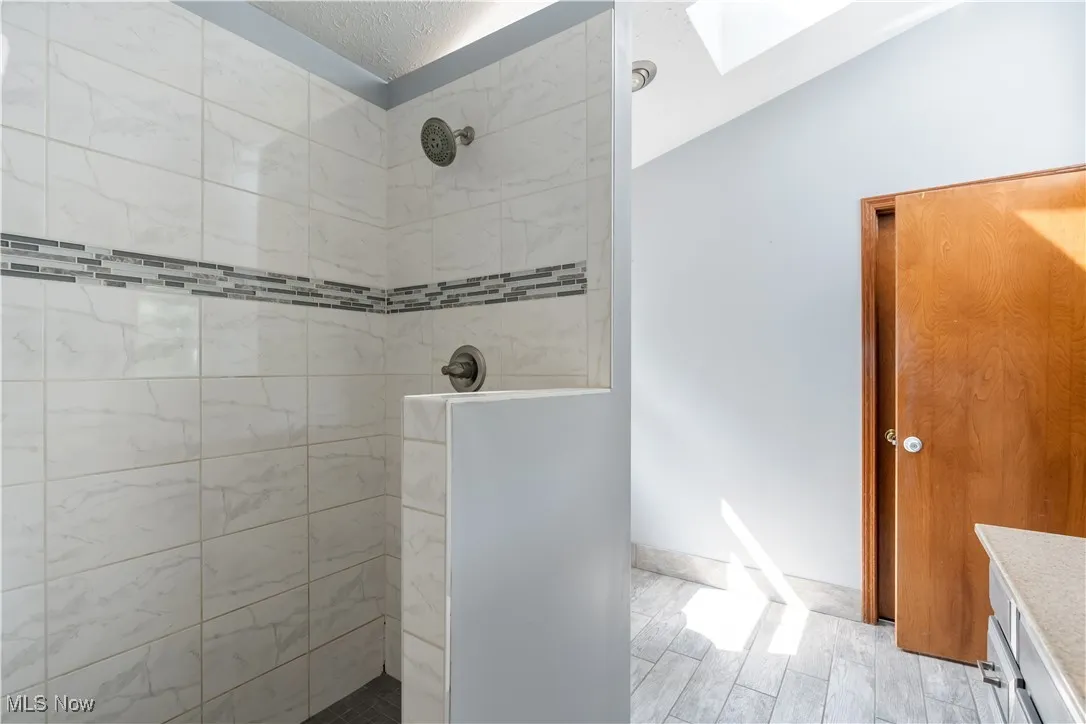 Bathroom featuring a walk in shower, a skylight, wood finished floors, vanity, and a textured ceiling