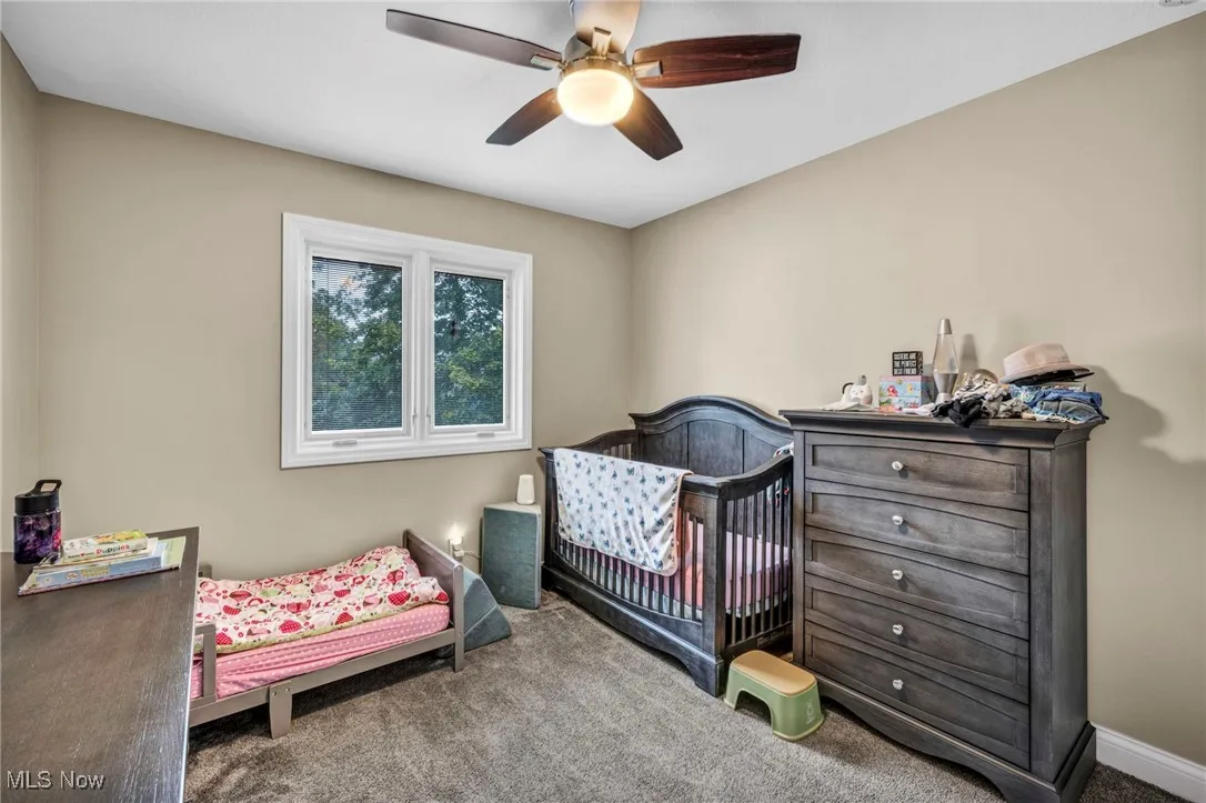 Carpeted bedroom with a ceiling fan and a nursery area