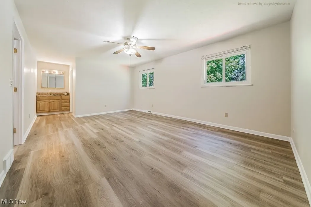 Unfurnished bedroom with light wood-type flooring, multiple windows, a ceiling fan, and ensuite bath