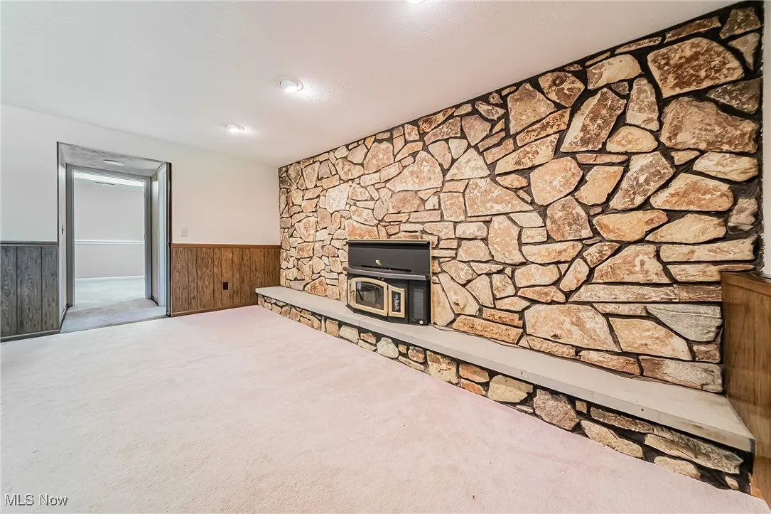 Unfurnished living room with a wainscoted wall, carpet floors, wooden walls, and a wood stove