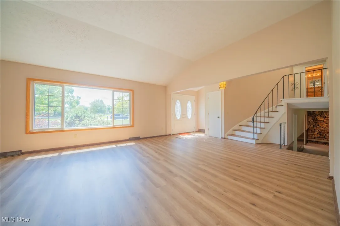 Unfurnished living room featuring plenty of natural light, wood finished floors, stairs, and vaulted ceiling